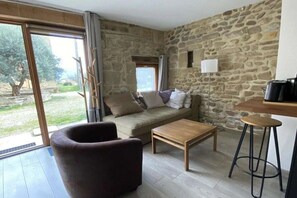 A room with a stone wall, a sofa, a wooden table, and a bar stool. - Holiday home with 1 bedroom (SAINT-LATTIER)