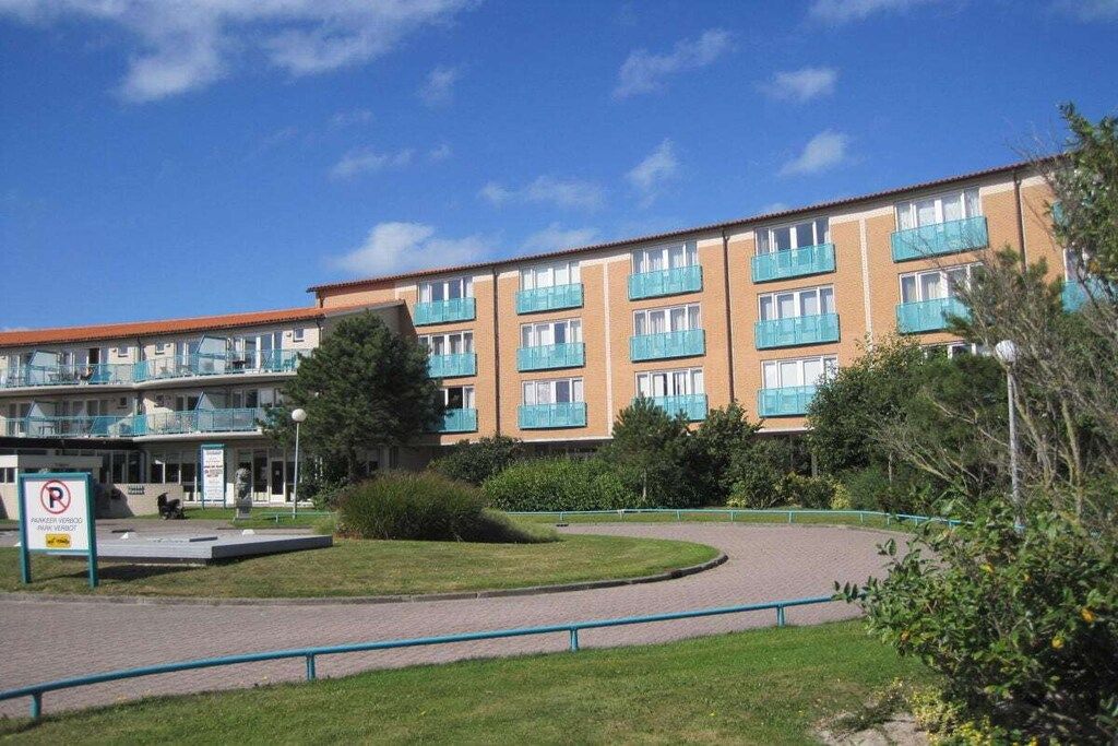 A multi-story building with balconies, a paved courtyard, and a no parking sign.