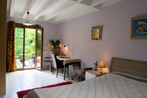 Ein Schlafzimmer mit einem Bett, einem Schreibtisch und einem Stuhl. Ein Fenster mit Vorhängen bietet Blick auf grüne Vegetation.