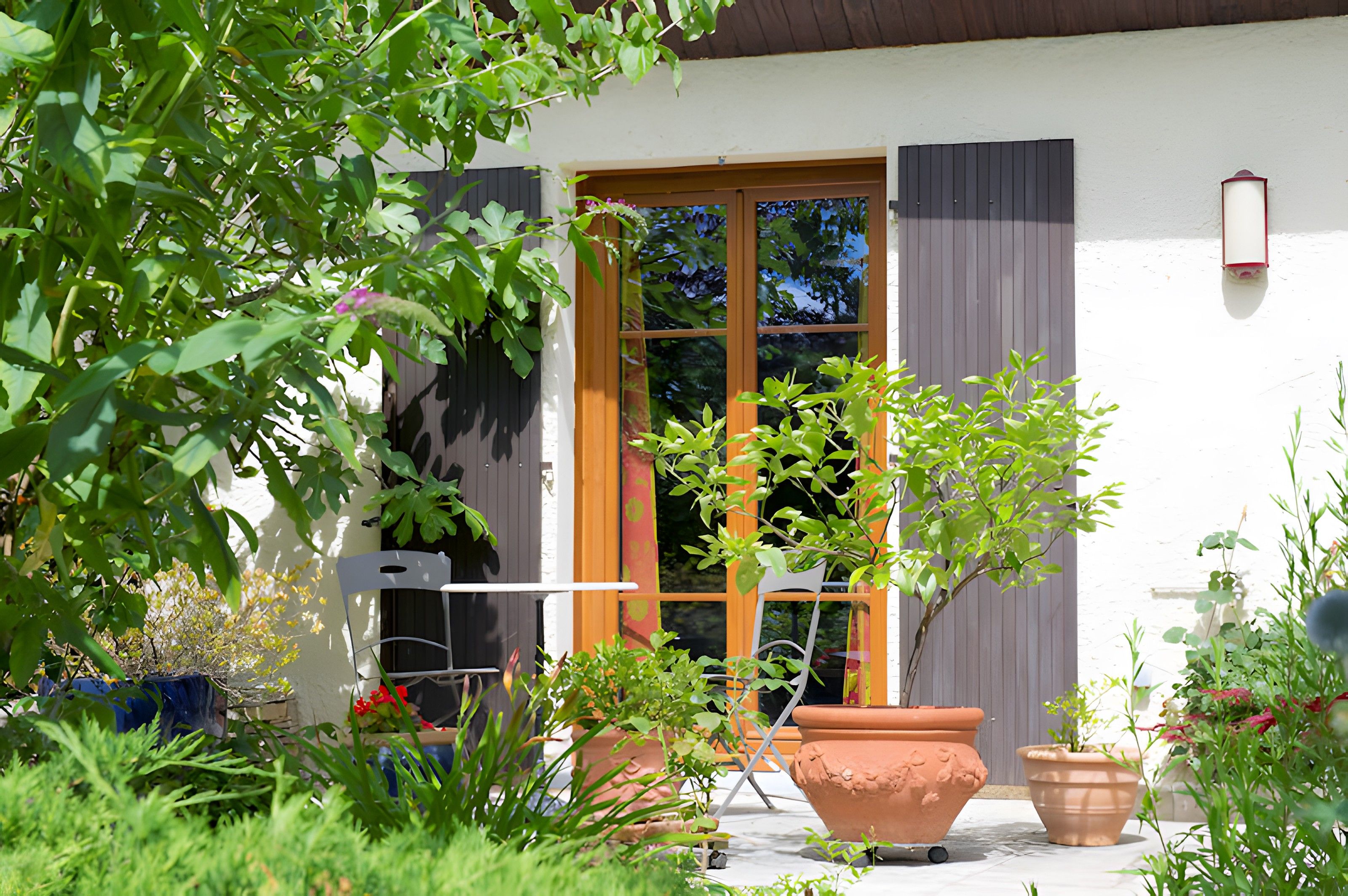 A patio with potted plants, a folding chair, and a window with curtains.