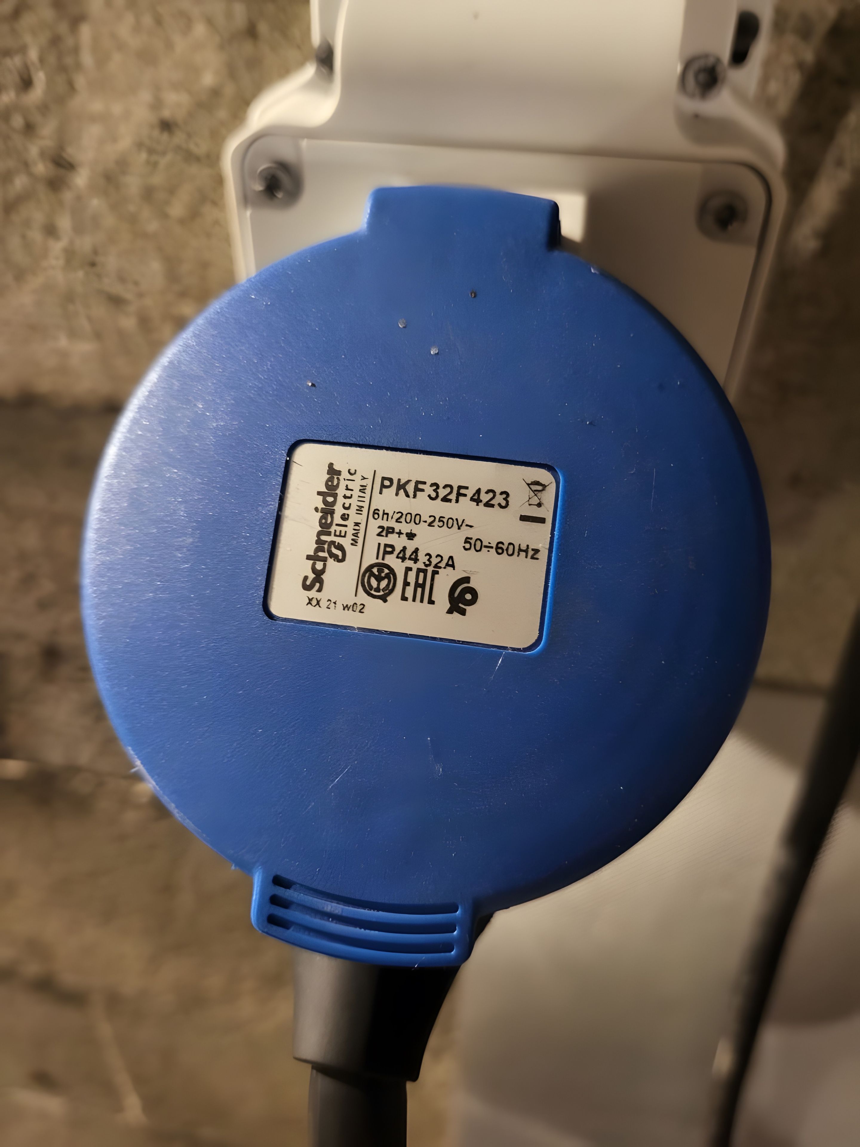 Une prise électrique bleue, portant une étiquette indiquant qu’il s’agit d’un produit Schneider Electric, modèle PKF32F423, avec les spécifications de tension et de fréquence.