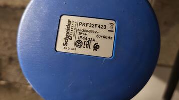 Une prise électrique bleue, portant une étiquette indiquant qu’il s’agit d’un produit Schneider Electric, modèle PKF32F423, avec les spécifications de tension et de fréquence.