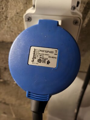 Ein blauer elektrischer Stecker mit einem Etikett, das angibt, dass es sich um ein Produkt von Schneider Electric handelt, Modell PKF32F423, zusammen mit Angaben zu Spannung und Frequenz.
