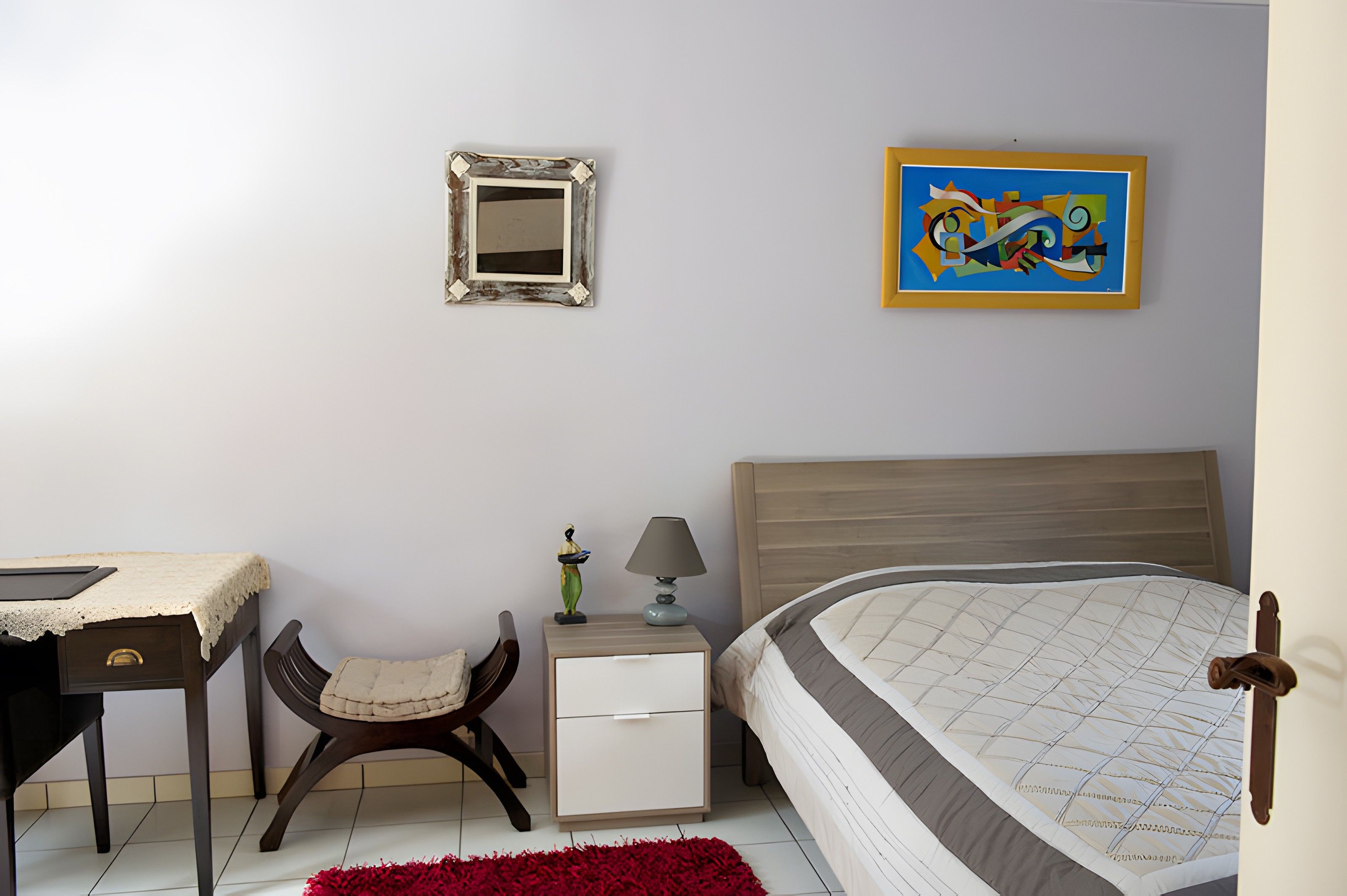 Une chambre à coucher comprenant un lit, une table de chevet, une chaise, une commode, un miroir et un tableau accroché au mur.