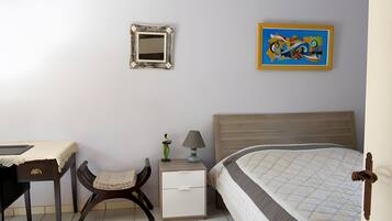 Une chambre à coucher comprenant un lit, une table de chevet, une chaise, une commode, un miroir et un tableau accroché au mur.