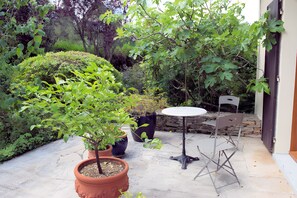 Eine Terrasse mit einem runden Tisch und zwei Stühlen, umgeben von Kübelpflanzen und einer Steinmauer.
