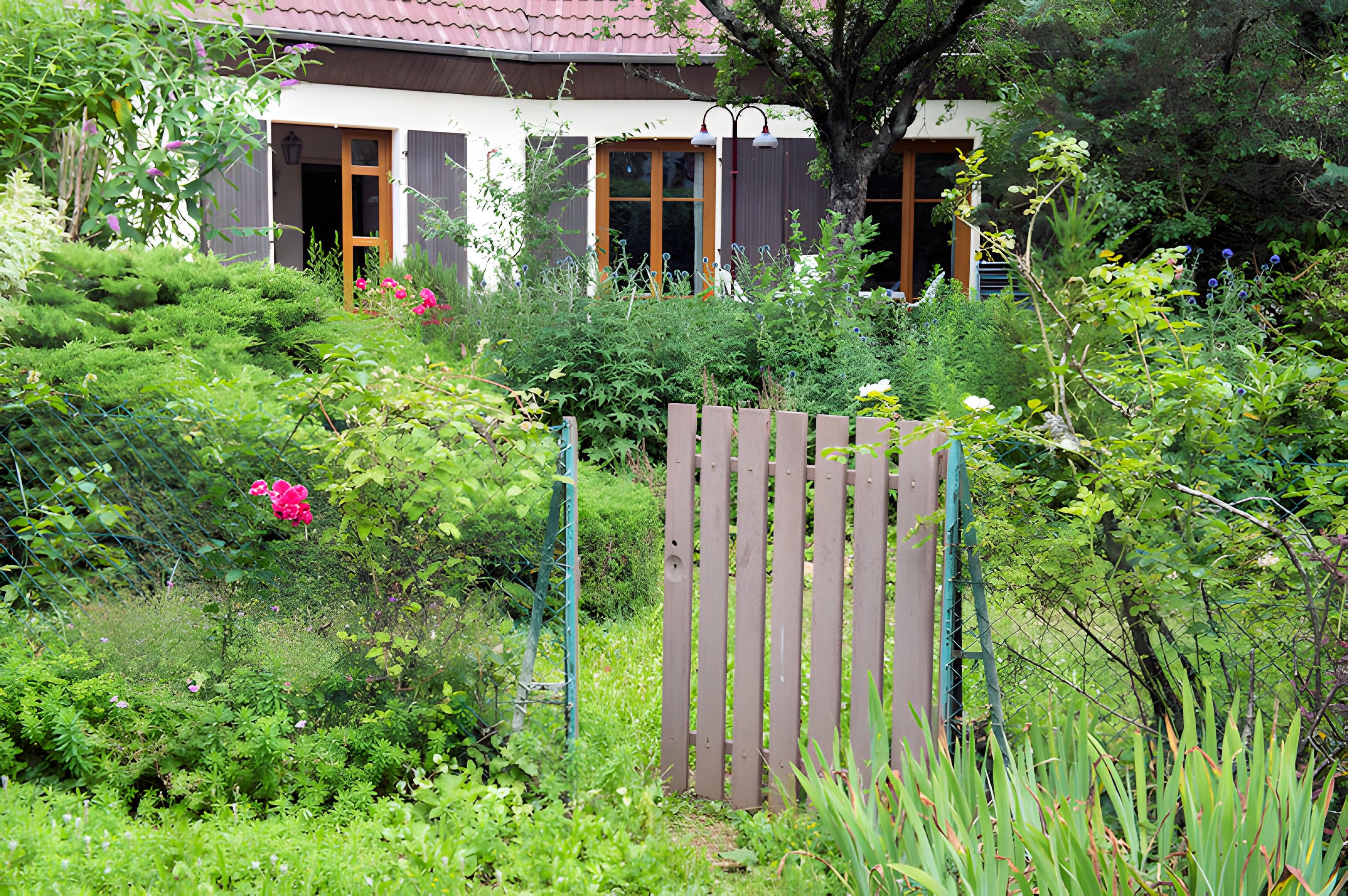 Il s’agit d’une propriété résidentielle dotée d’un jardin, d’une clôture en bois et d’une maison avec un toit rouge.