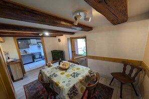 Ein Essbereich mit einem Tisch, der mit einer gemusterten Tischdecke bedeckt ist, Holzstühlen und einer rustikalen Decke.