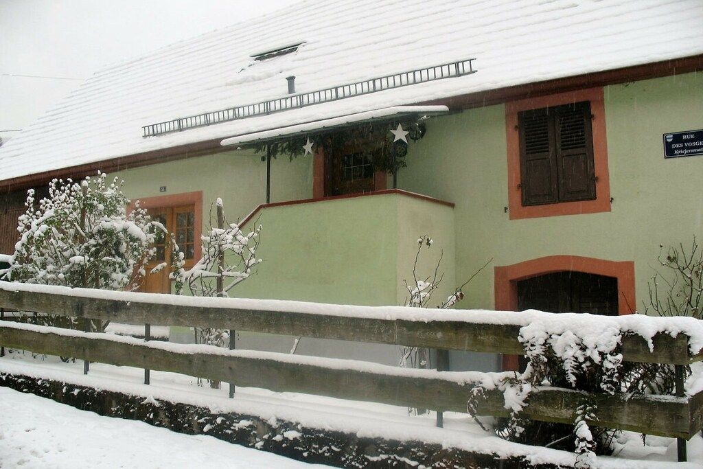 A building with a green facade, a wooden fence, and snow-covered surroundings.