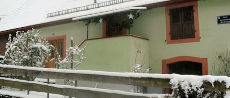 A building with a green facade, a wooden fence, and snow-covered surroundings.