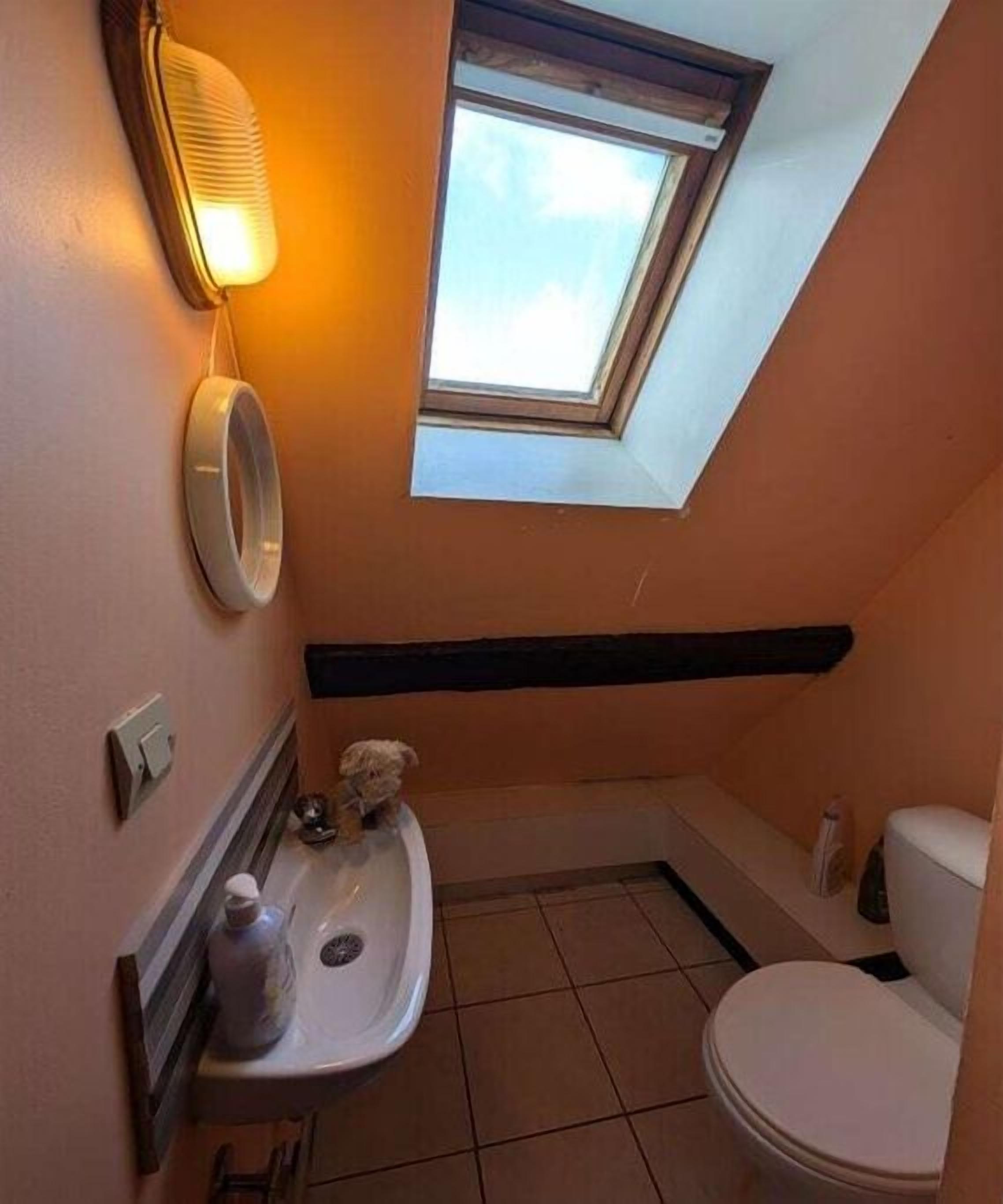 Un baño pequeño con tragaluz, inodoro, lavamanos y espejo.