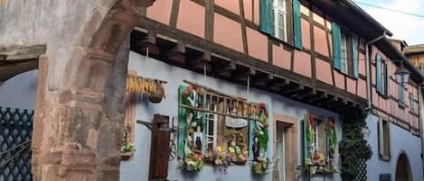 A traditional half-timbered building with a stone archway, a cobblestone street, and hanging flower baskets.
