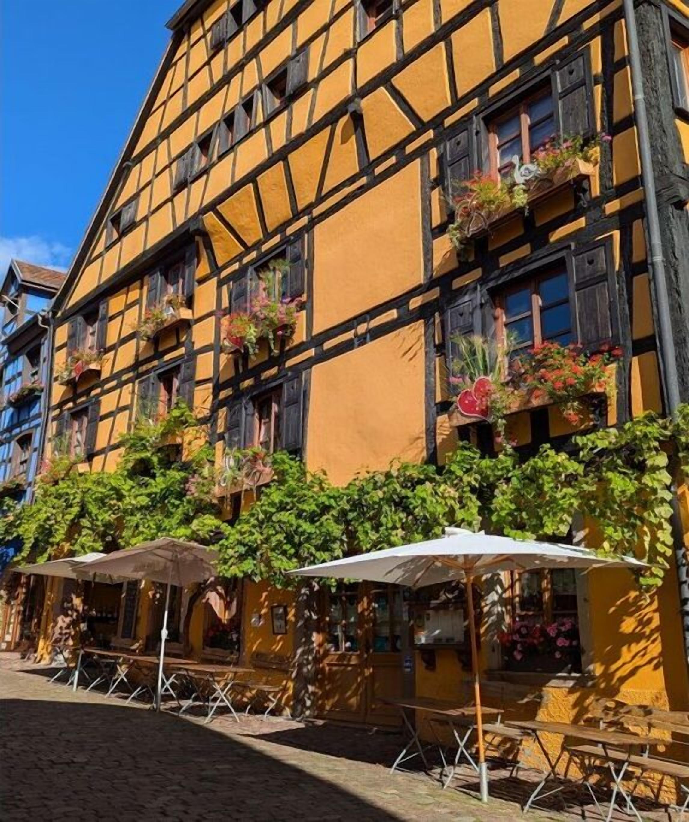 Un bâtiment traditionnel à colombages, doté d’une terrasse et de jardinières fleuries.
