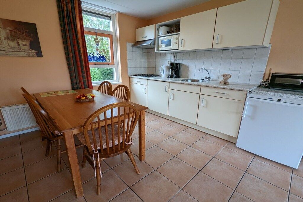 A kitchen with a dining table, chairs, a refrigerator, and a window with curtains.