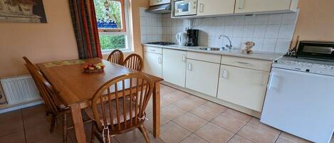 A kitchen with a dining table, chairs, a refrigerator, and a window with curtains.