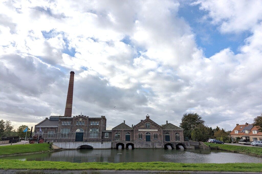 A historic building with a tall chimney, a canal, and a bridge connecting to another structure.