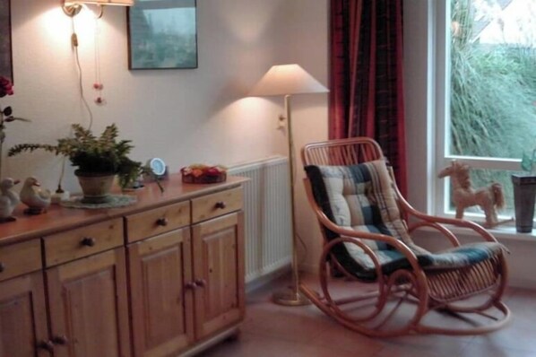 A room with a wooden cabinet, a wicker chair, a floor lamp, and a window with curtains. - Holiday home with 1 bedroom (Medemblik)