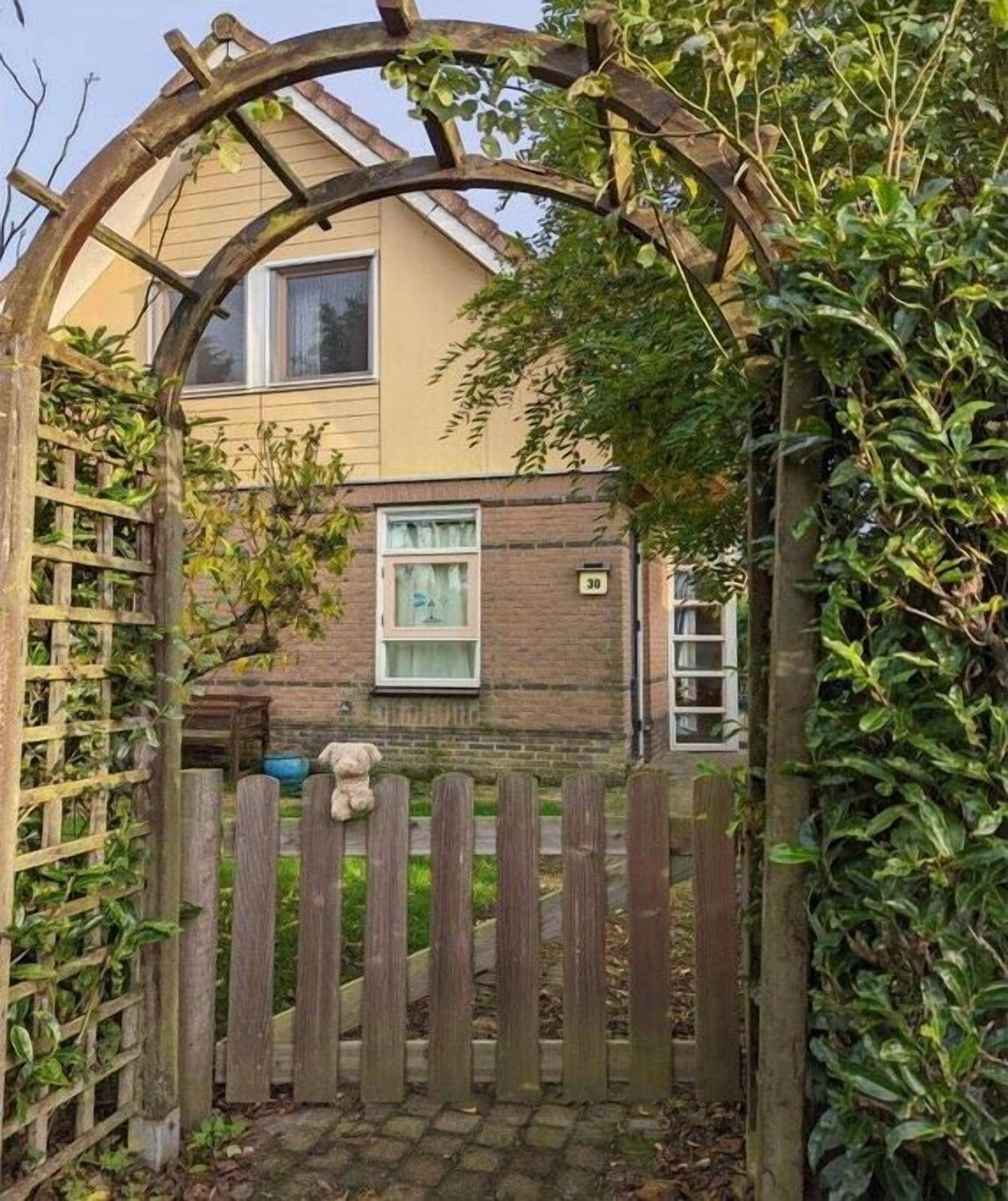 A wooden gate leading to a house with a brick facade, a window, and a small porch area.