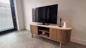 Een moderne woonkamer met een flatscreen televisie op een houten standaard, een afstandsbediening en een witte vaas.