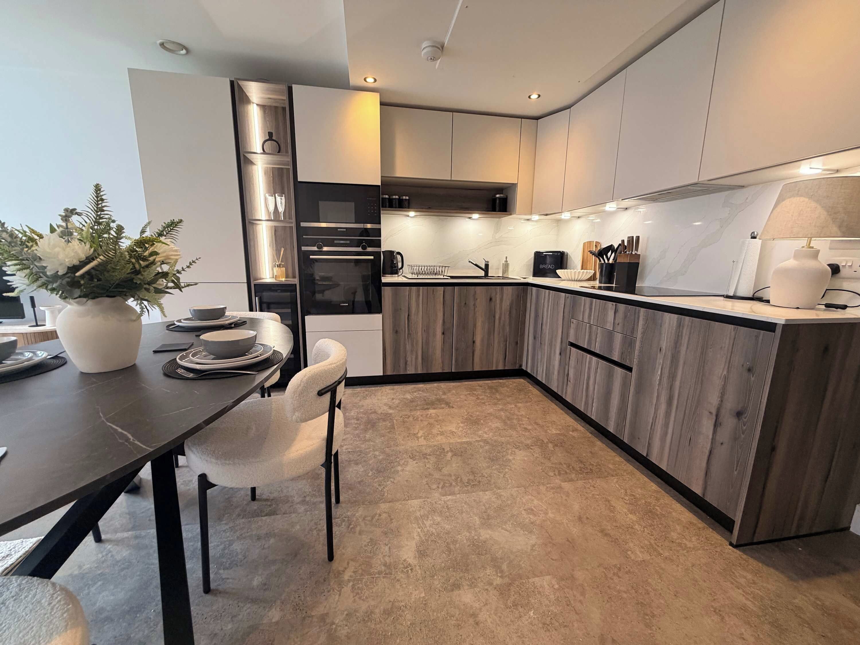 A modern kitchen with wooden cabinets, a built-in oven, and a dining area with a table and chairs.