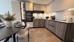 Een moderne keuken met houten kastjes, een inbouwoven en een eethoek met een tafel en stoelen.