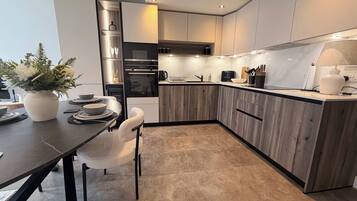 A modern kitchen with wooden cabinets, a built-in oven, and a dining area with a table and chairs.