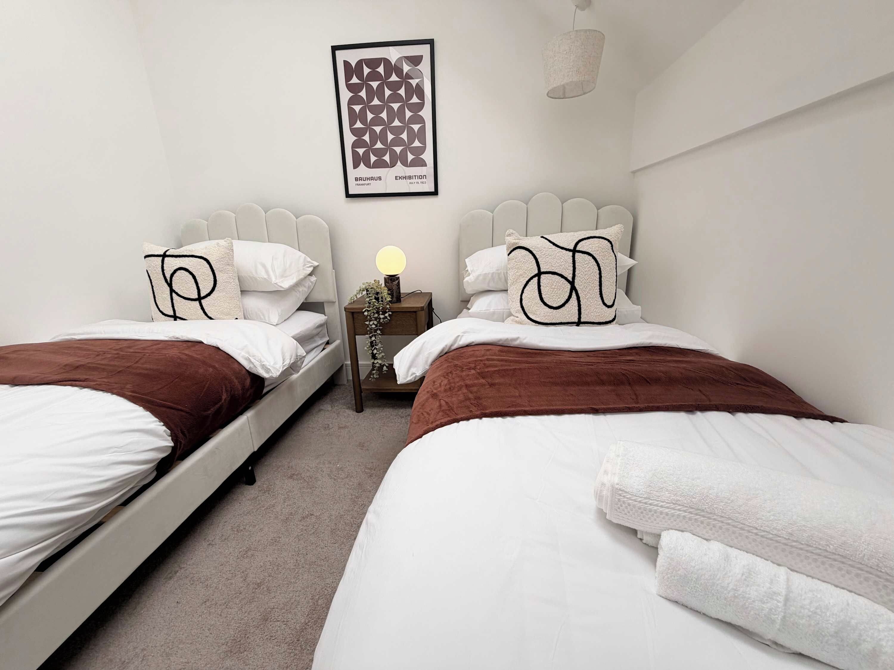 A hotel room with two beds, a nightstand with a lamp, and a framed picture on the wall.