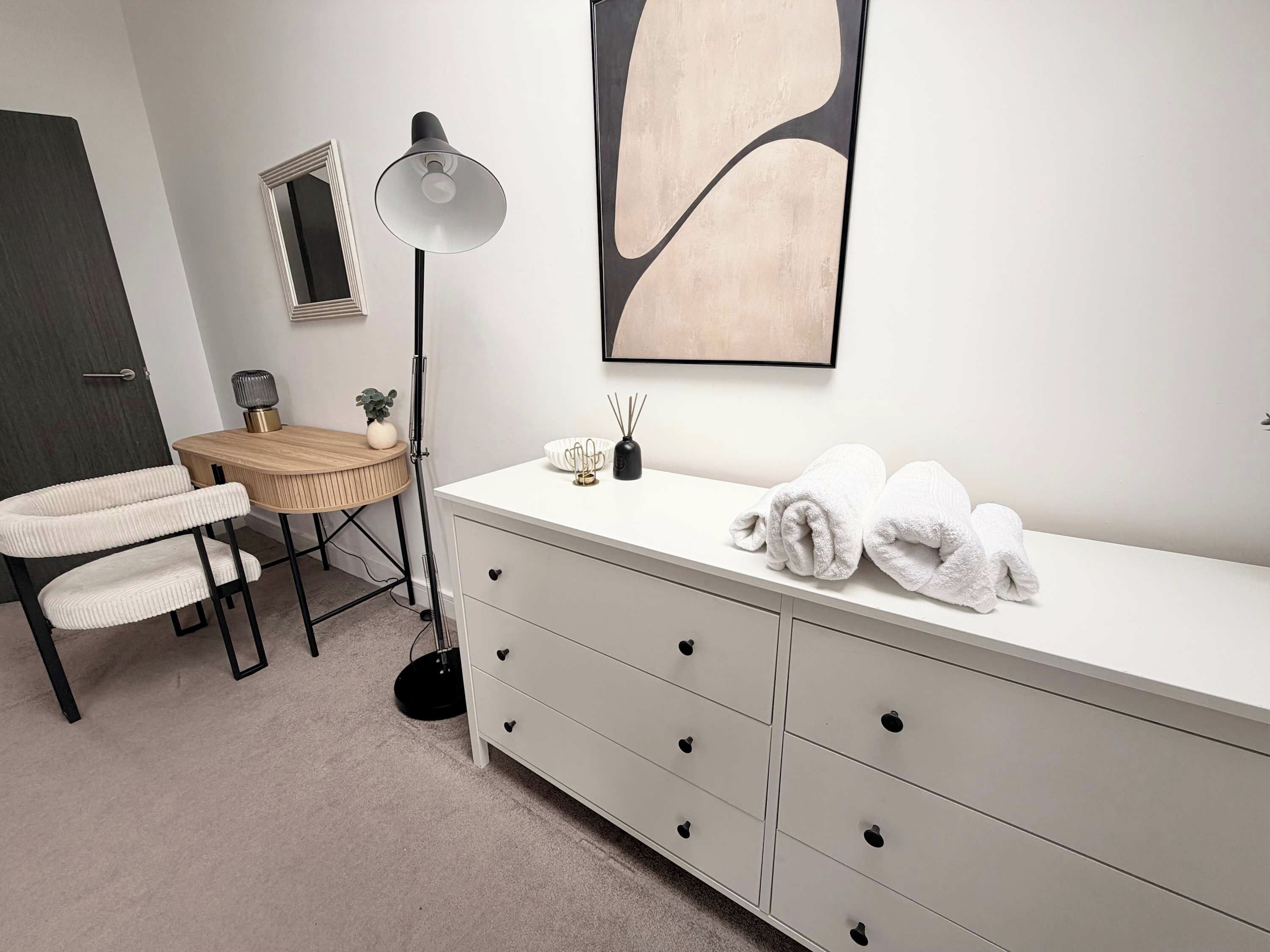 Une salle de bain moderne avec un meuble-lavabo blanc, un miroir rond, un lampadaire et un grand tableau abstrait accroché au mur.