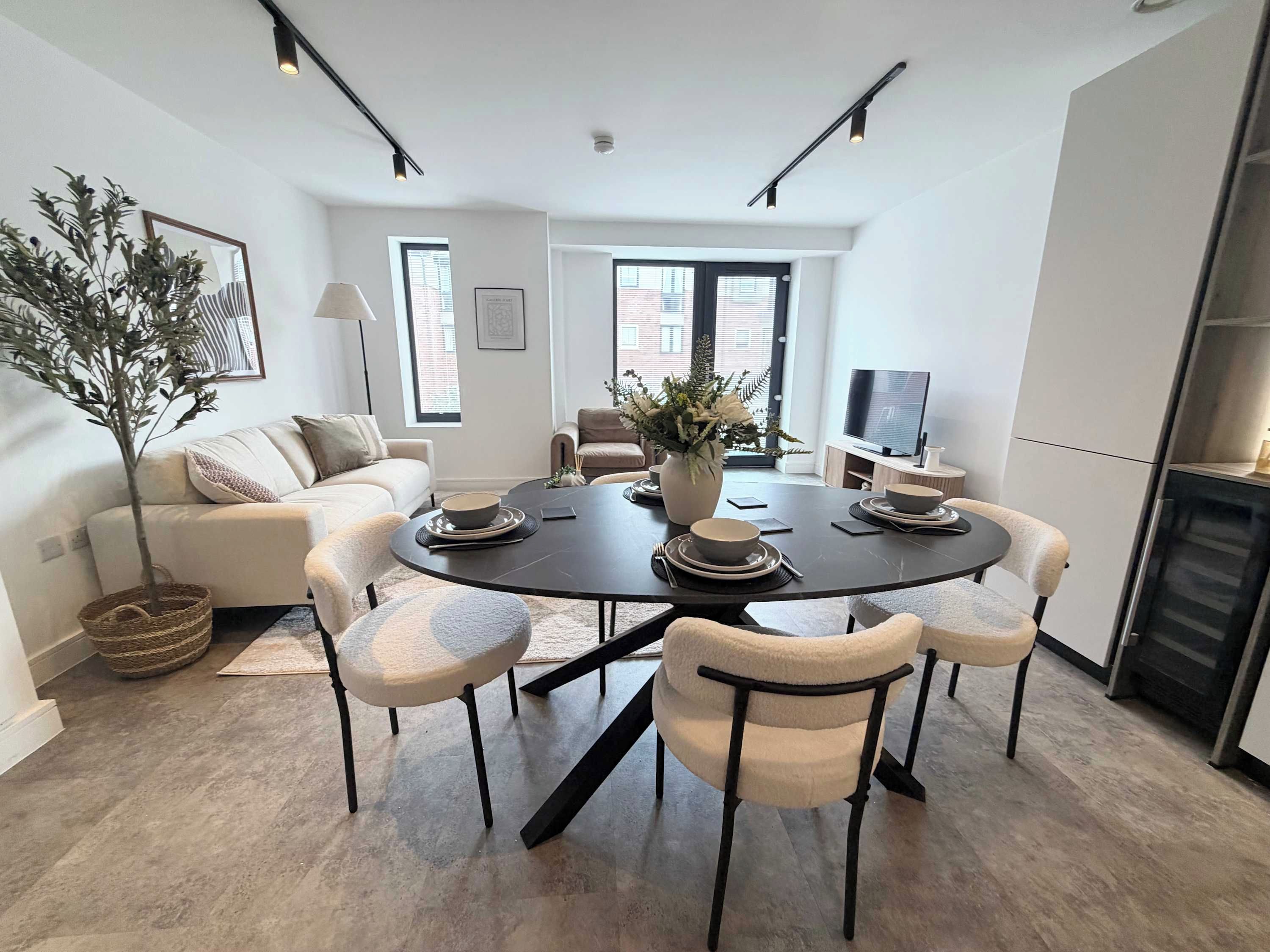 A modern dining area with a round table, six chairs, and a vase of flowers.