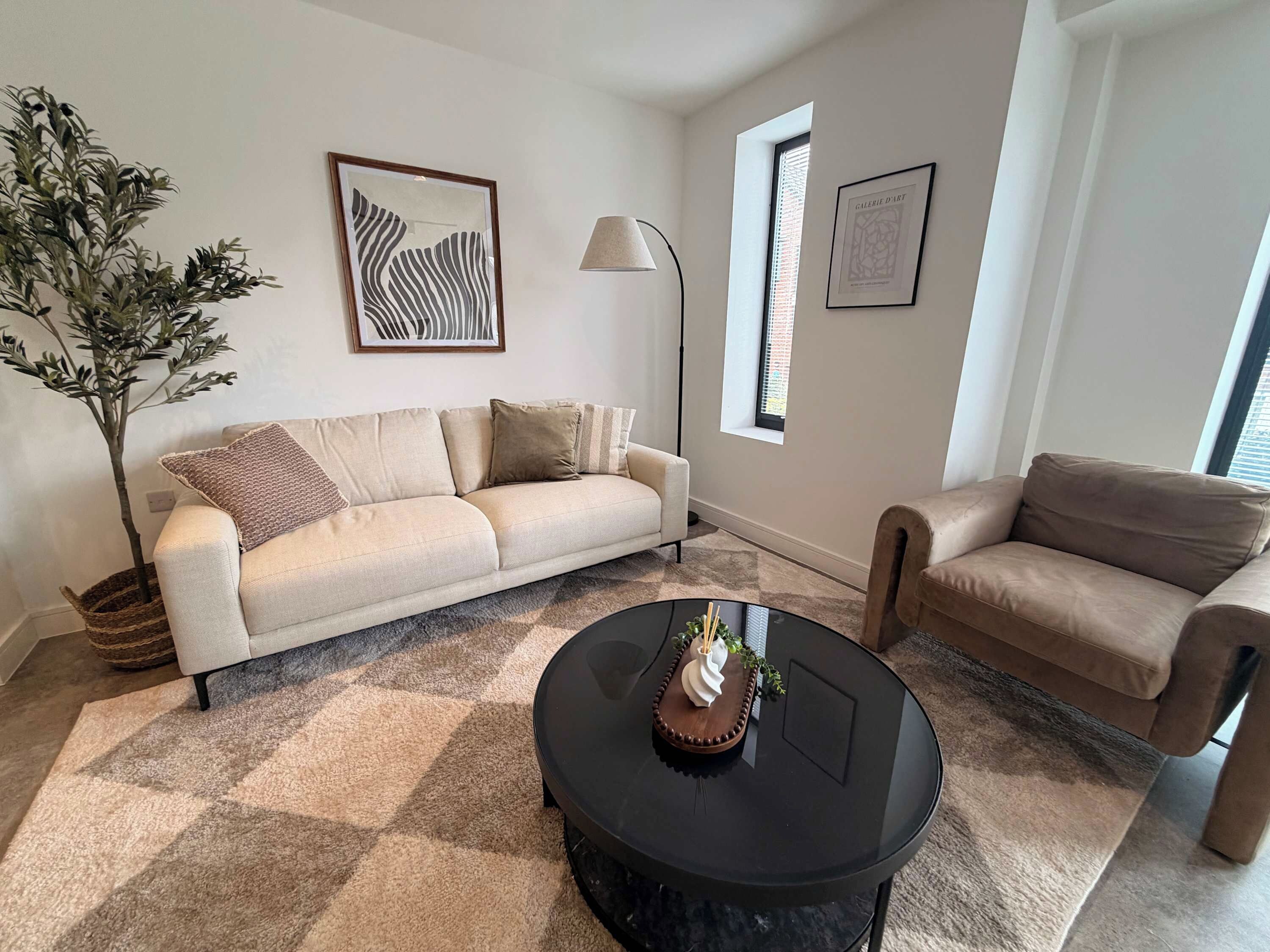 A living room with a beige sofa, a round black coffee table, and a potted plant.
