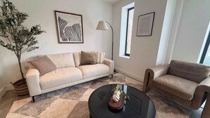 Een woonkamer met een beige bank, een ronde zwarte salontafel en een kamerplant.