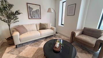 A living room with a beige sofa, a round black coffee table, and a potted plant.