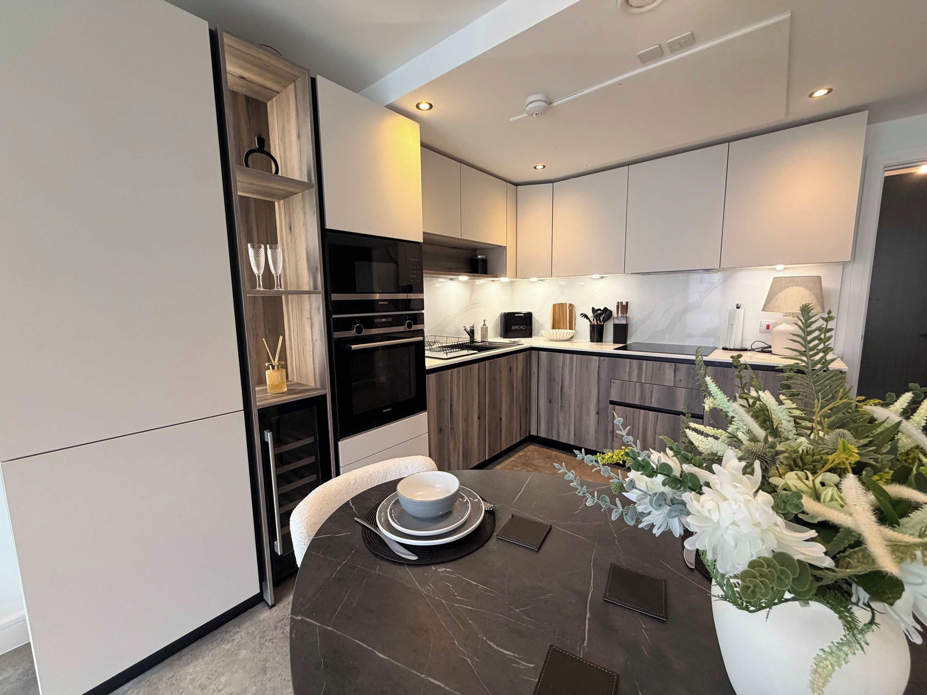 A modern kitchen with built-in appliances, a dining table set for two, and a decorative plant.