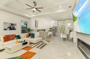 A modern living room with a sofa, coffee table, and a TV screen displaying a beach scene. - New! Wave Chaser • New Luxury Build • Heated Salt Pool/Spa • 1 Mile to Vanderbilt Beach! (Naples)