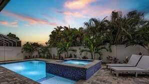 A swimming pool with a tiled edge, surrounded by a brick patio. There are lounge chairs and a small hot tub. - New! Wave Chaser • New Luxury Build • Heated Salt Pool/Spa • 1 Mile to Vanderbilt Beach! (Naples)