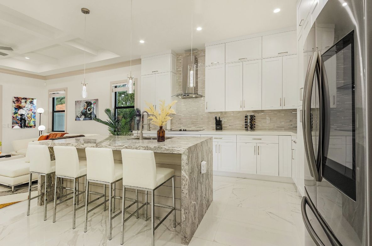 Una cocina moderna con una isla de mármol, armarios blancos y electrodomésticos de acero inoxidable.