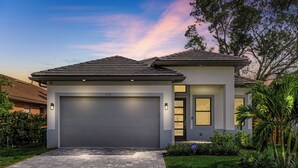 A modern two-story house with a garage, a driveway, and a well-maintained lawn. - New! Wave Chaser • New Luxury Build • Heated Salt Pool/Spa • 1 Mile to Vanderbilt Beach! (Naples)
