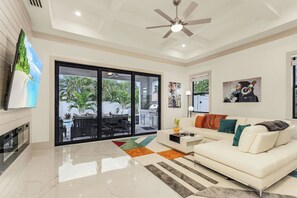 A modern living room with a white sofa, a coffee table, and a large window with a view of outdoor furniture. - New! Wave Chaser • New Luxury Build • Heated Salt Pool/Spa • 1 Mile to Vanderbilt Beach! (Naples)