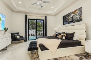 Ein Schlafzimmer mit einem großen Bett, einem Deckenventilator, einem Gemälde und Blick ins Freie.
