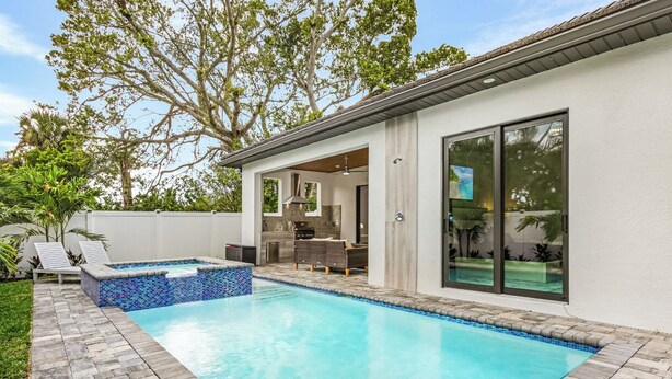 A modern house with a swimming pool, outdoor seating, and a large window. - New! Wave Chaser • New Luxury Build • Heated Salt Pool/Spa • 1 Mile to Vanderbilt Beach! (Naples)