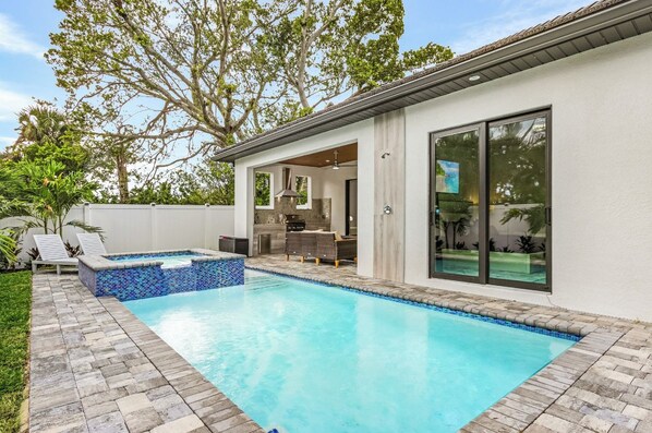 Ein modernes Haus mit Swimmingpool, Sitzgelegenheit im Freien und einem großen Fenster.