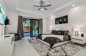 Ein modernes Schlafzimmer mit einem großen Bett, Nachttischlampen, einem Deckenventilator und Blick auf einen Swimmingpool.