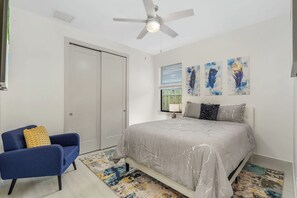 Ein Schlafzimmer mit einem Bett, einem Sessel, einem Deckenventilator und Kunstwerken an der Wand.