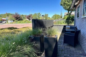 A courtyard with outdoor seating, a brick building, and a road with a traffic island. - Holiday apartment with 1 bedroom (Oudkarspel)