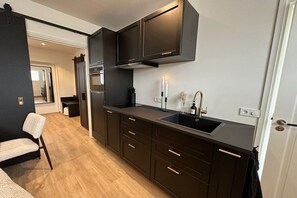 A modern kitchen with dark cabinetry, a stainless steel sink, and a built-in oven. - Holiday apartment with 1 bedroom (Oudkarspel)