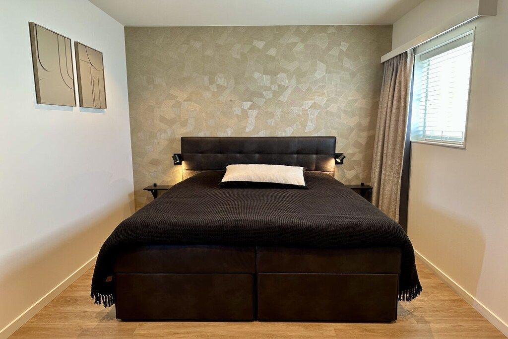 A bedroom with a large bed, a headboard, bedside tables, and a window with curtains.