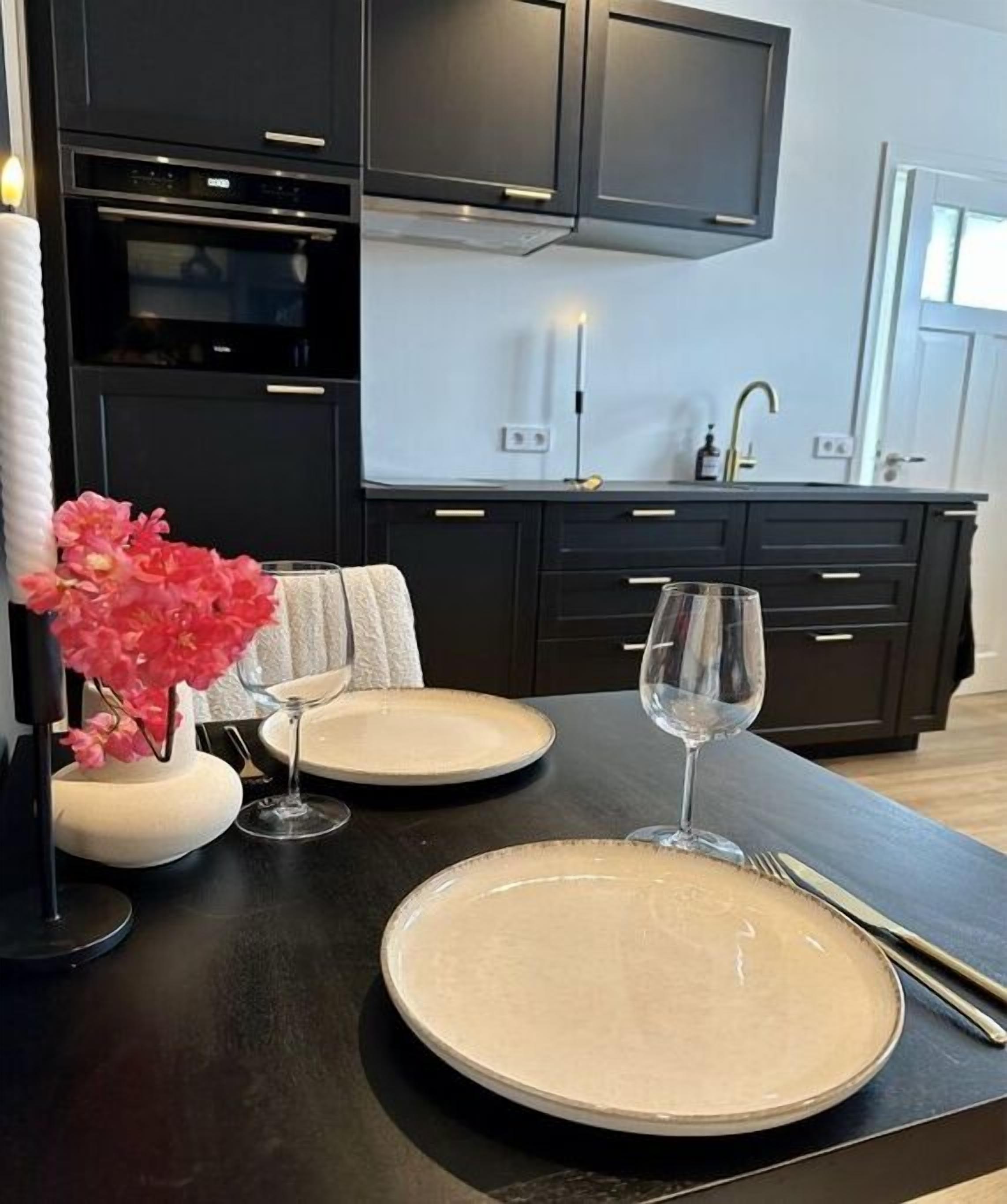 A modern kitchen with dark cabinetry, a built-in oven, and a dining area with a table set for two.