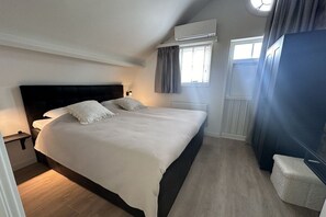 Ein Schlafzimmer mit einem großen Bett, einem Nachttisch, einem Fenster mit Vorhängen und einer Klimaanlage.