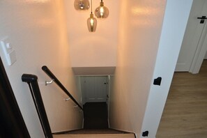 A staircase with a handrail, a light fixture above, and a door at the bottom. - Holiday apartment with 3 bedrooms (Oudkarspel)