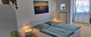 A bedroom with a bed, two bedside tables with lamps, a painting on the wall, a radiator, and a view of the outside. - BergNah Piding Vacation Rental – Light-Filled with 6 Balconies + Mountain Views (Piding)
